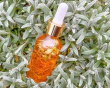 Load image into Gallery viewer, 2 oz glass bottle of body oil with a dropper. The bottle is filled with a yellow-hued oil, and it appears to be infused with botanical elements.